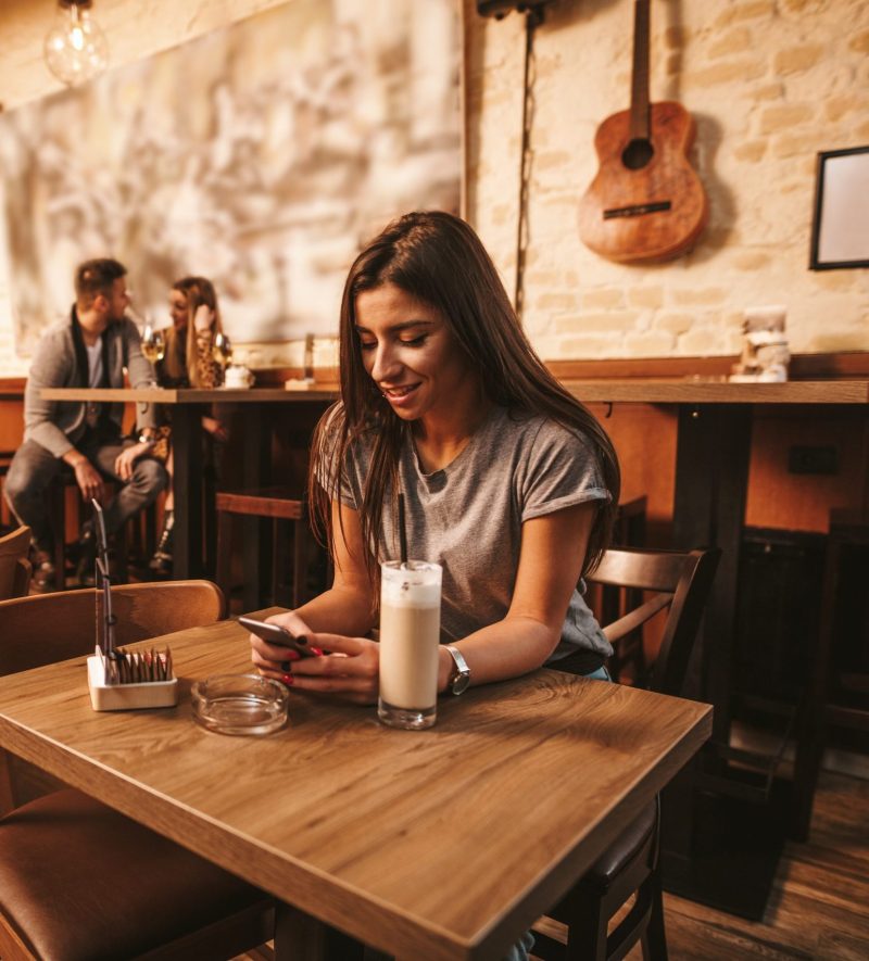 Attractive young woman is reading good news on smartphone while is sitting at cafe.