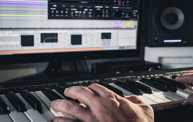 A music producer working with a midi keyboard synthesizer and a computer