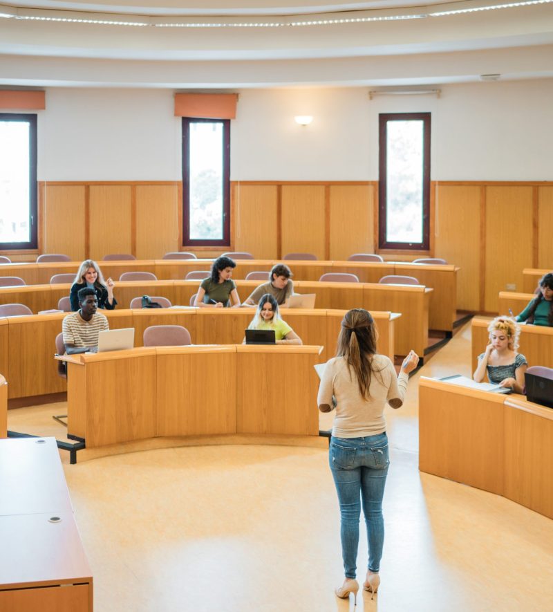 High angle of woman explaining task to group of students with laptops during lesson in light auditorium of modern university